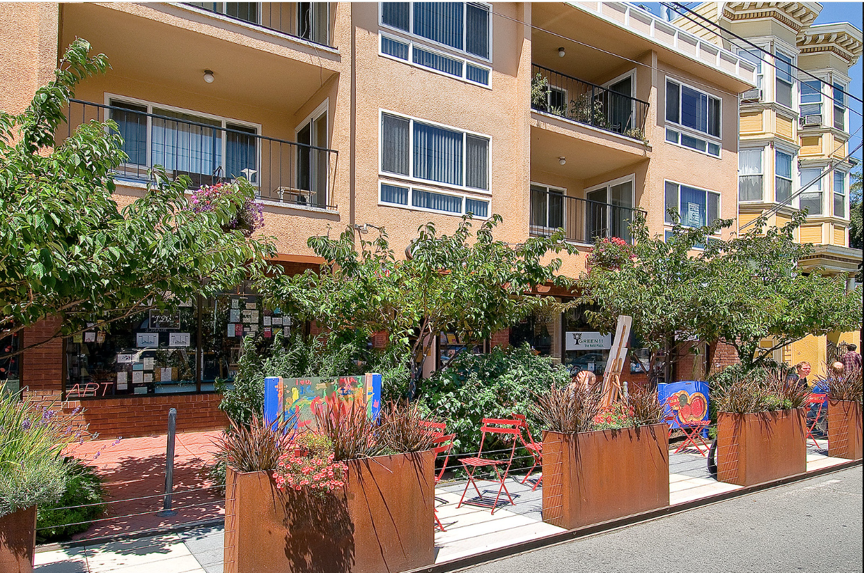 Apartment courtyard with potted flowers, trees, and blue patio chairs along a brick walkway
