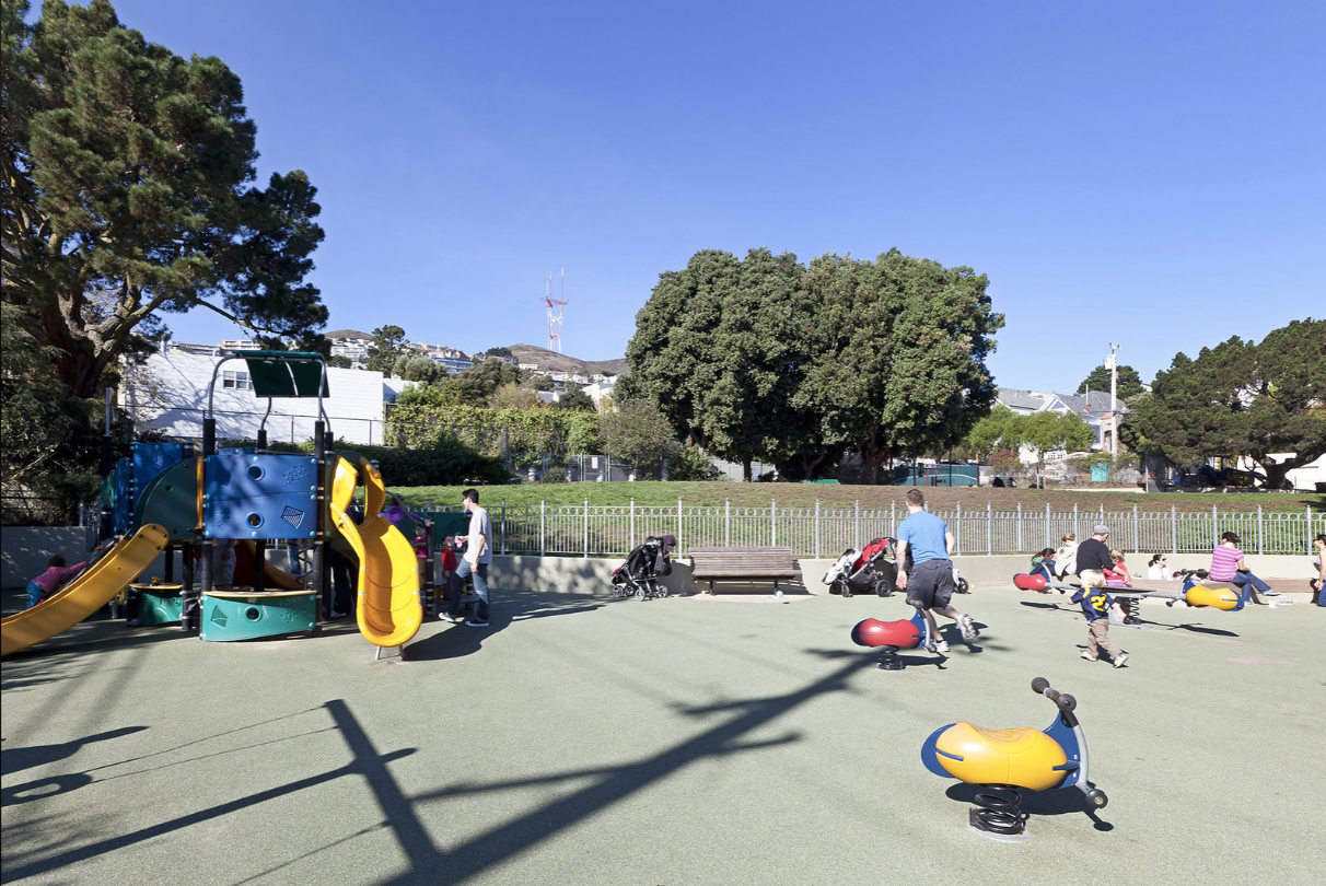 Children playing on a sunny playground with slides, climbing structures, and benches in the background.