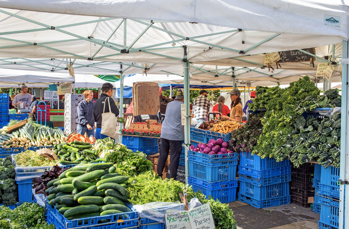 Outdoor market stall with colorful fresh produce in blue crates under white tents