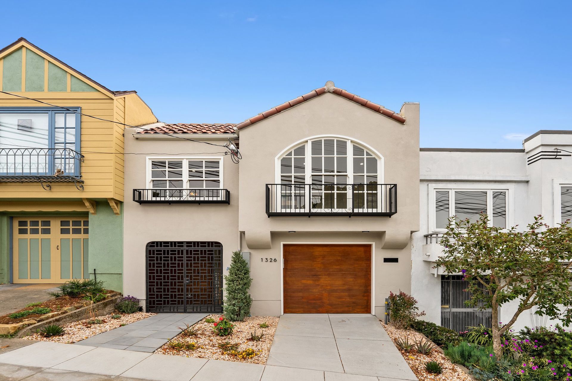 Row of modern townhouses with balconies, garage doors, and front steps under a clear blue sky