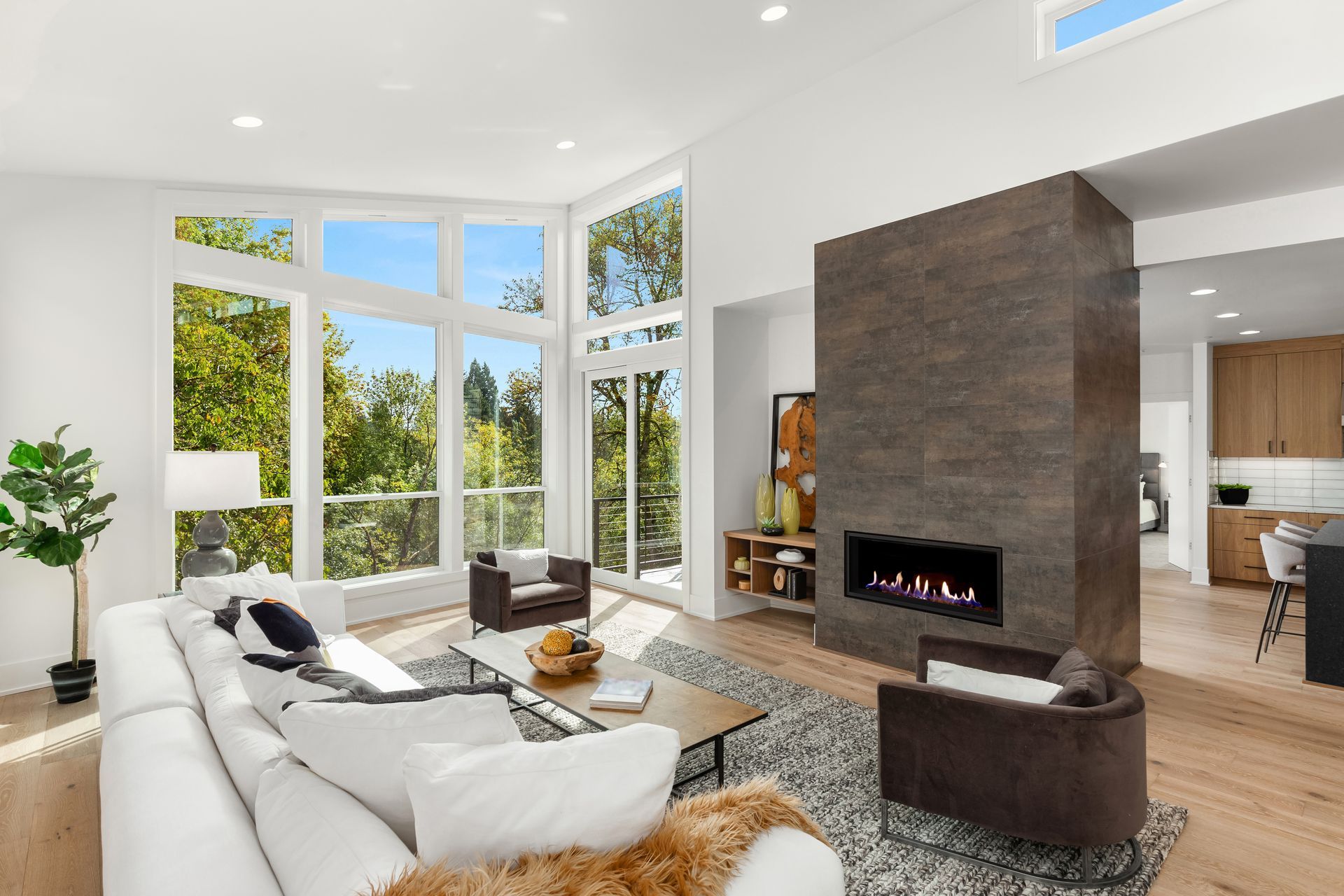 Bright modern living room with white sofa, large windows, and a tall stone fireplace.