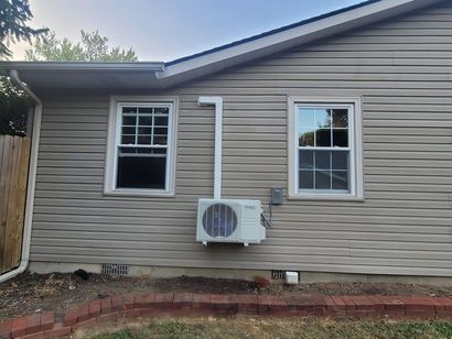 Exterior wall of a house with two windows and an air conditioning unit.