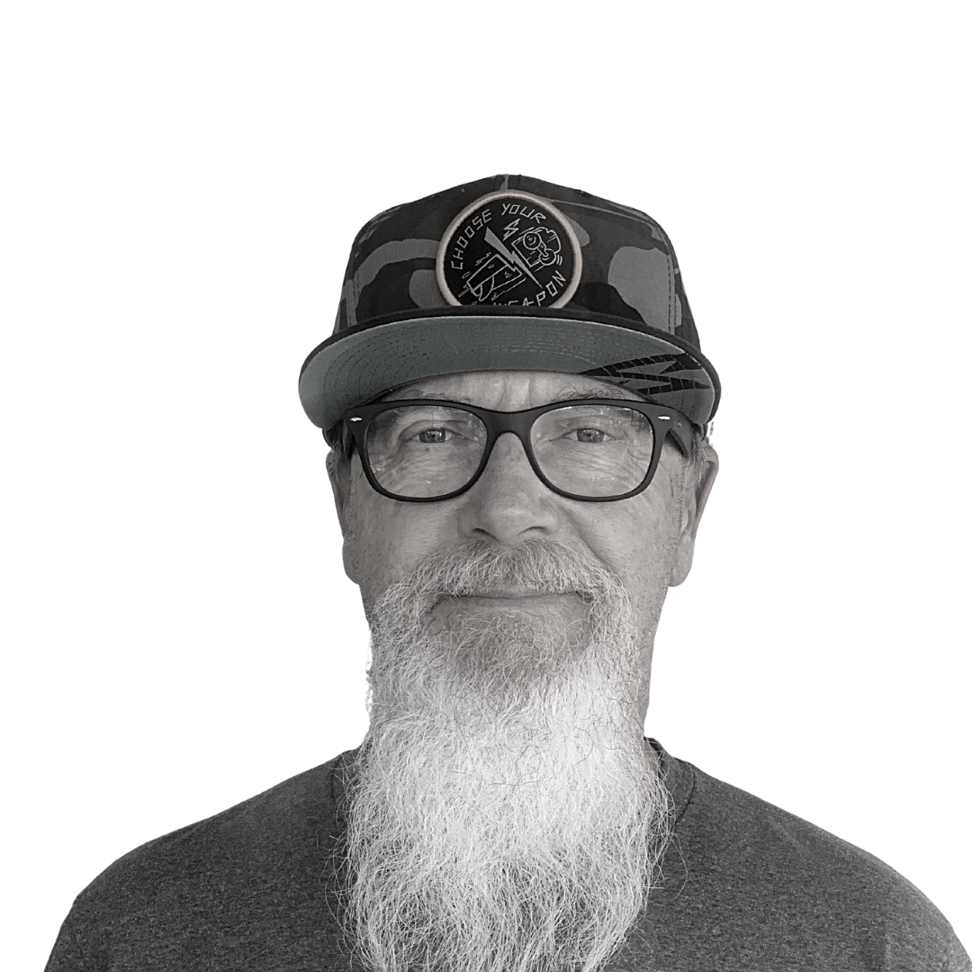 Portrait of a man wearing glasses and a cap, with a long gray beard, against a plain background