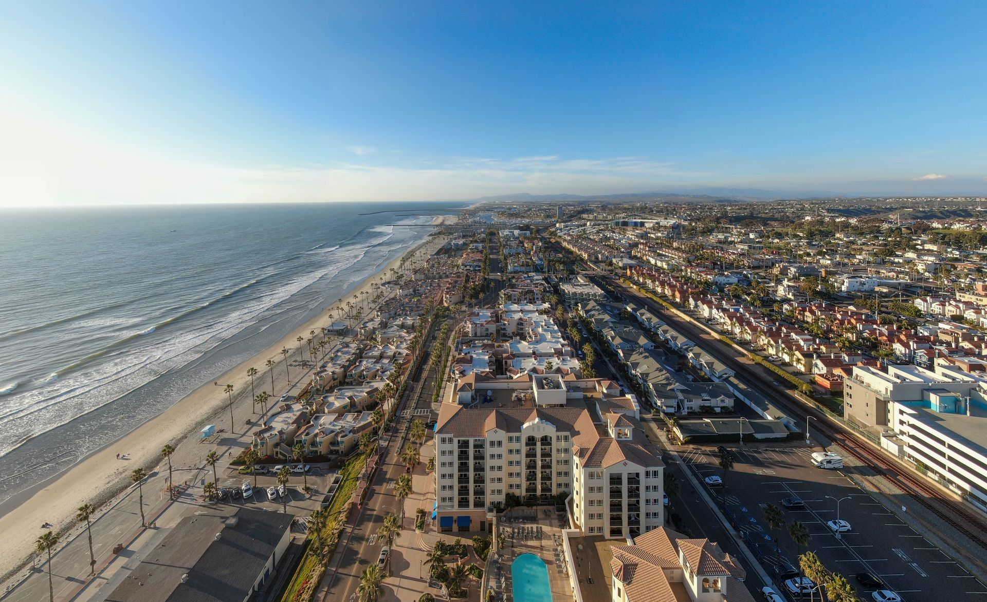 Aerial view of a sandy beachfront and coastal city along the ocean under a clear sky.