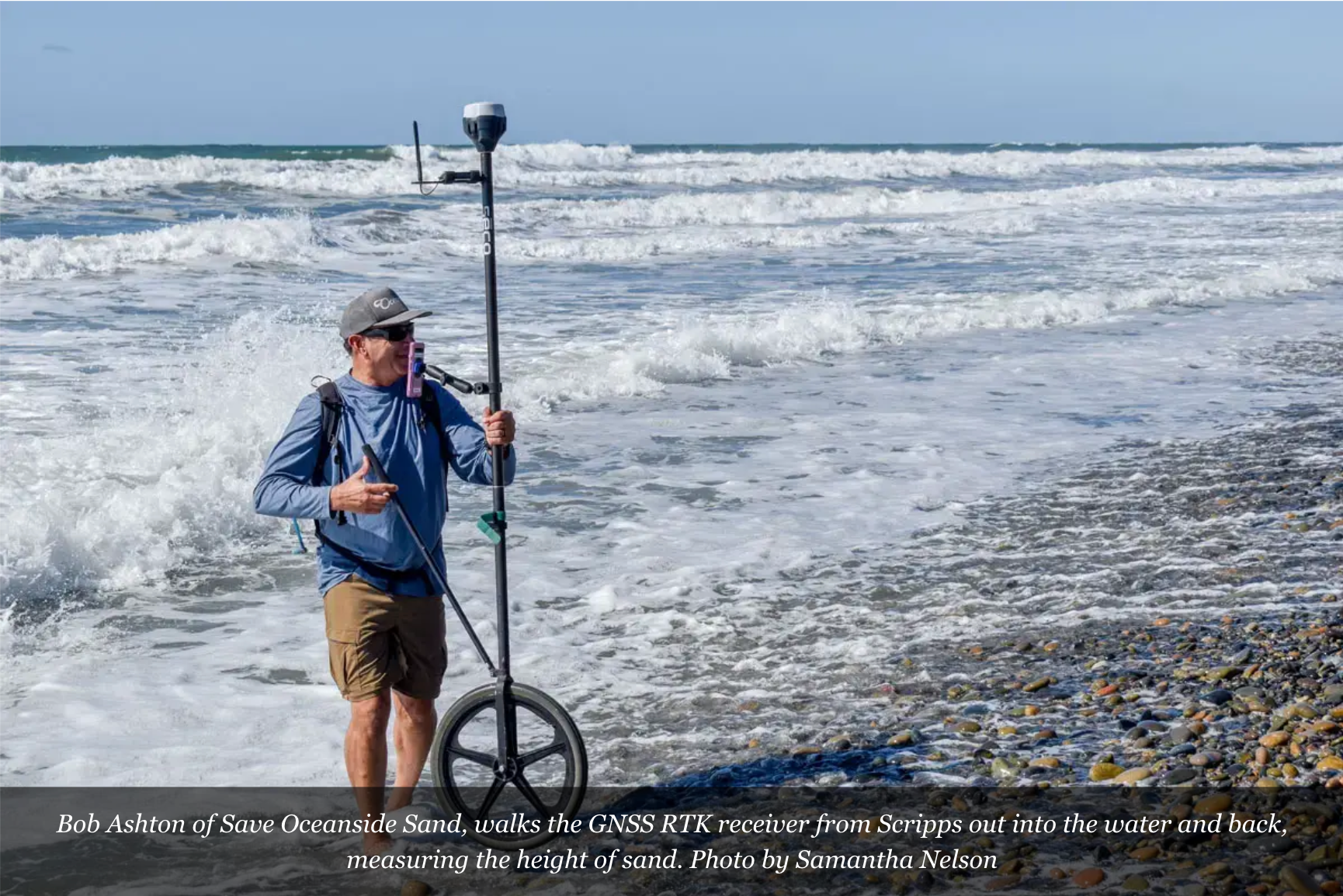 Man standing on a rocky shoreline holding a pole beside choppy ocean waves