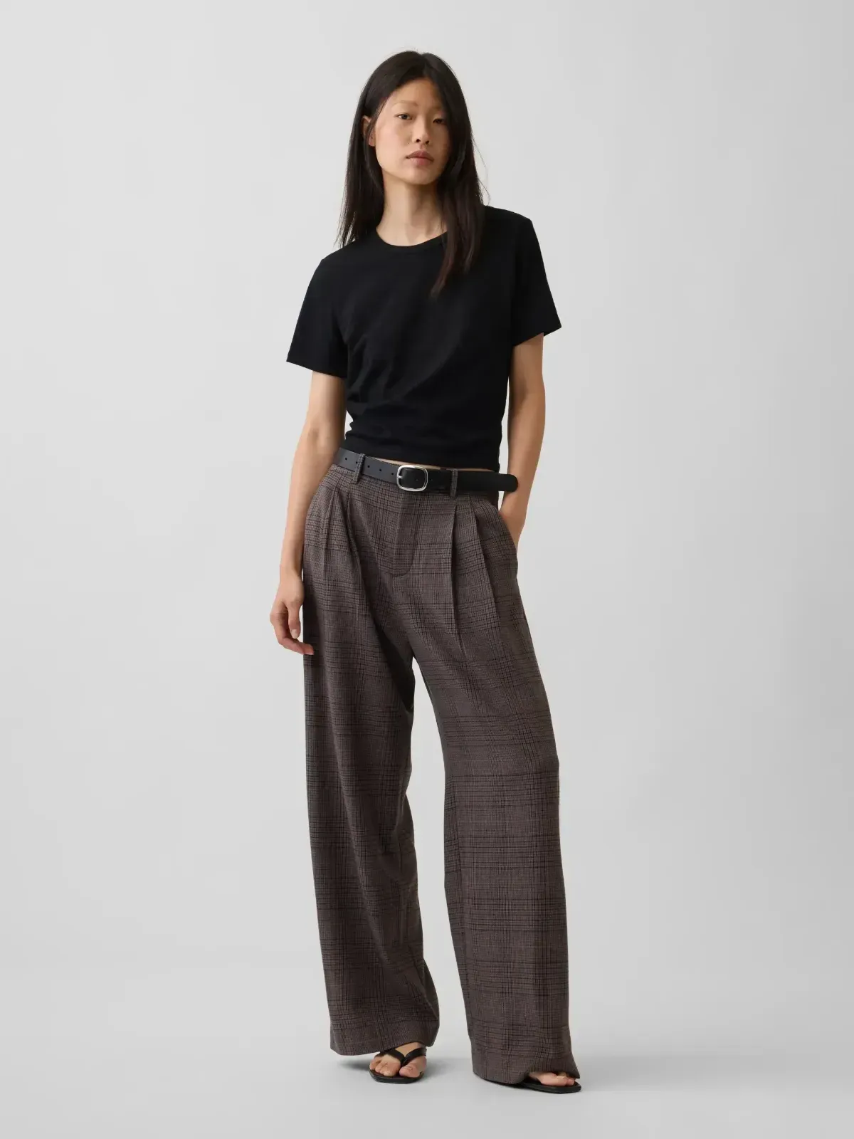 Woman standing in a black T-shirt and patterned wide-leg pants against a plain light background