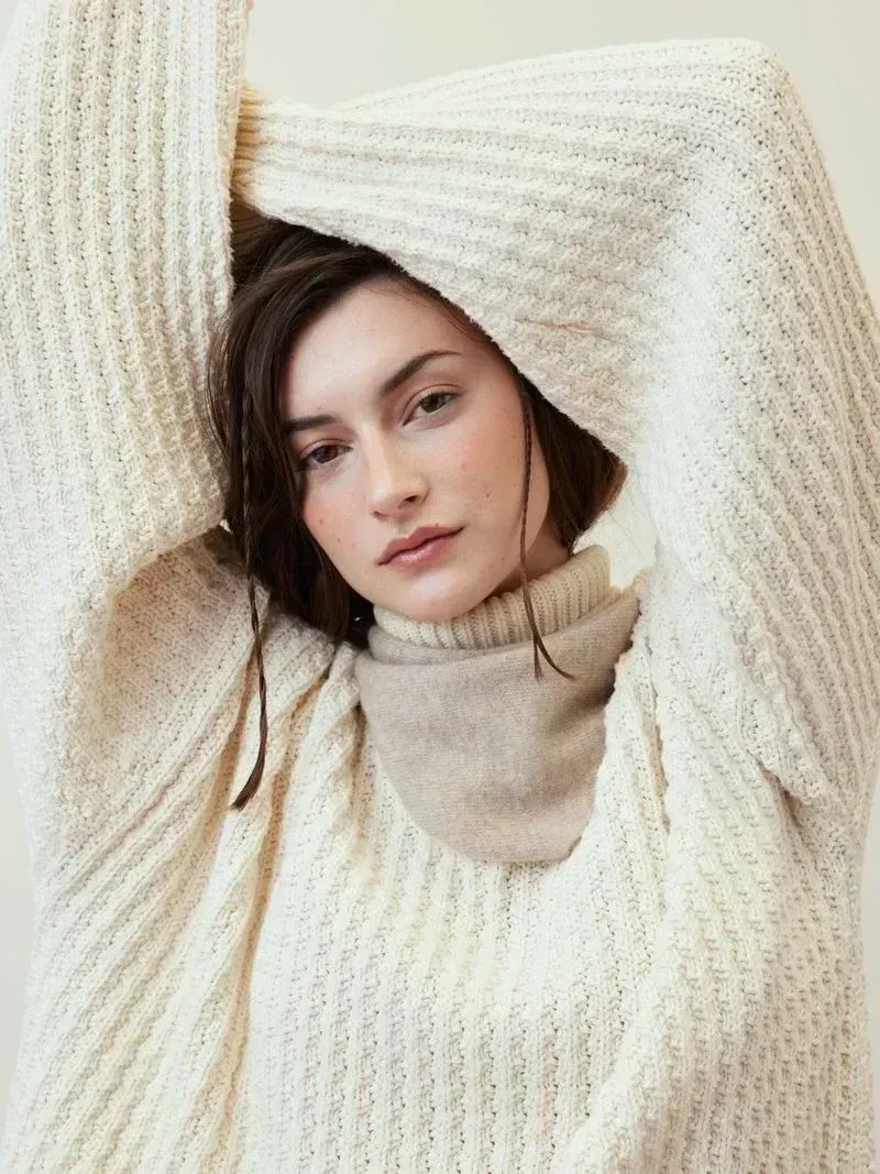 Model wearing an oversized cream sweater and satin skirt in a soft studio pose