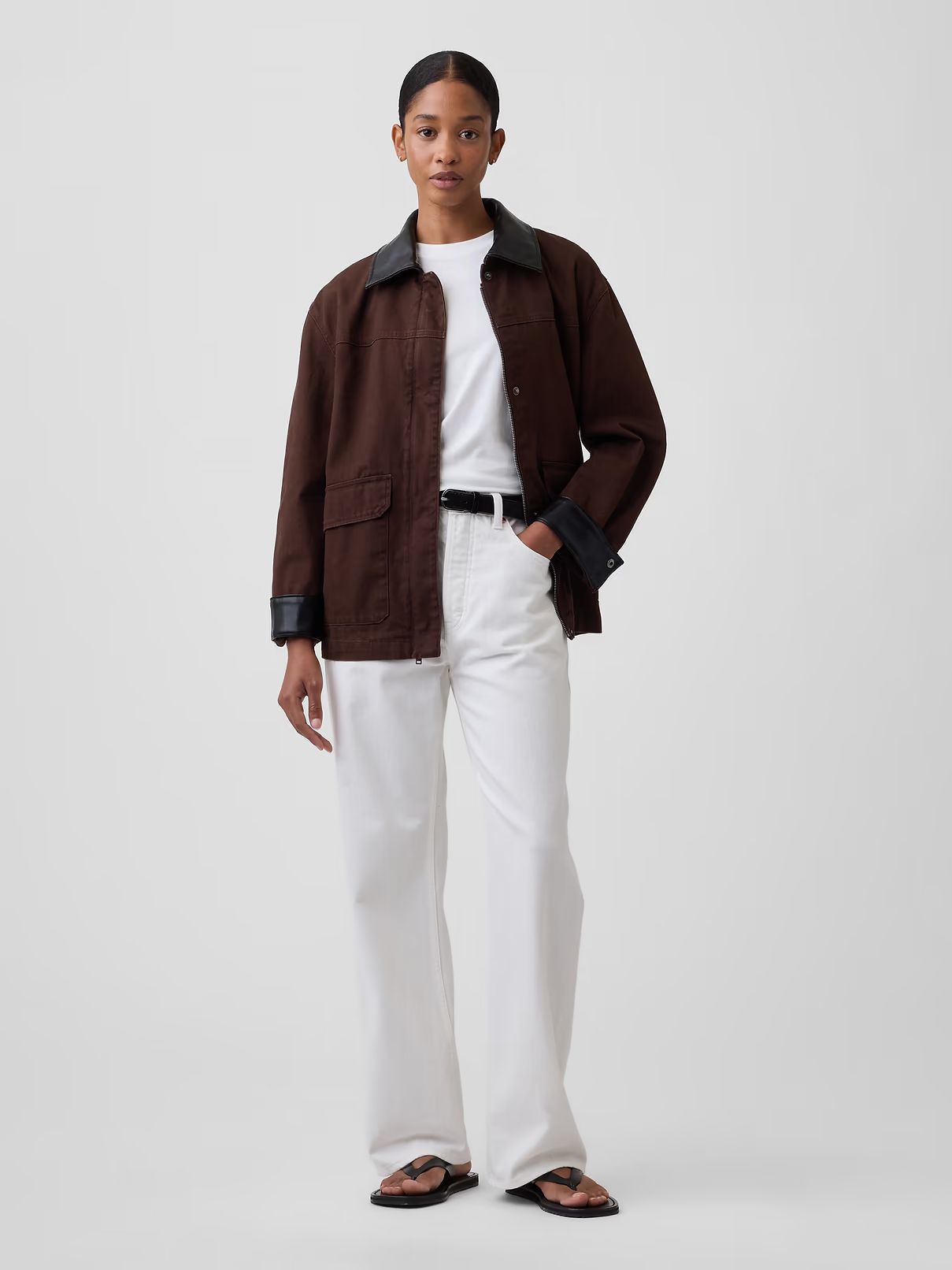 Model in a brown jacket, white shirt and trousers, standing against a light gray background.