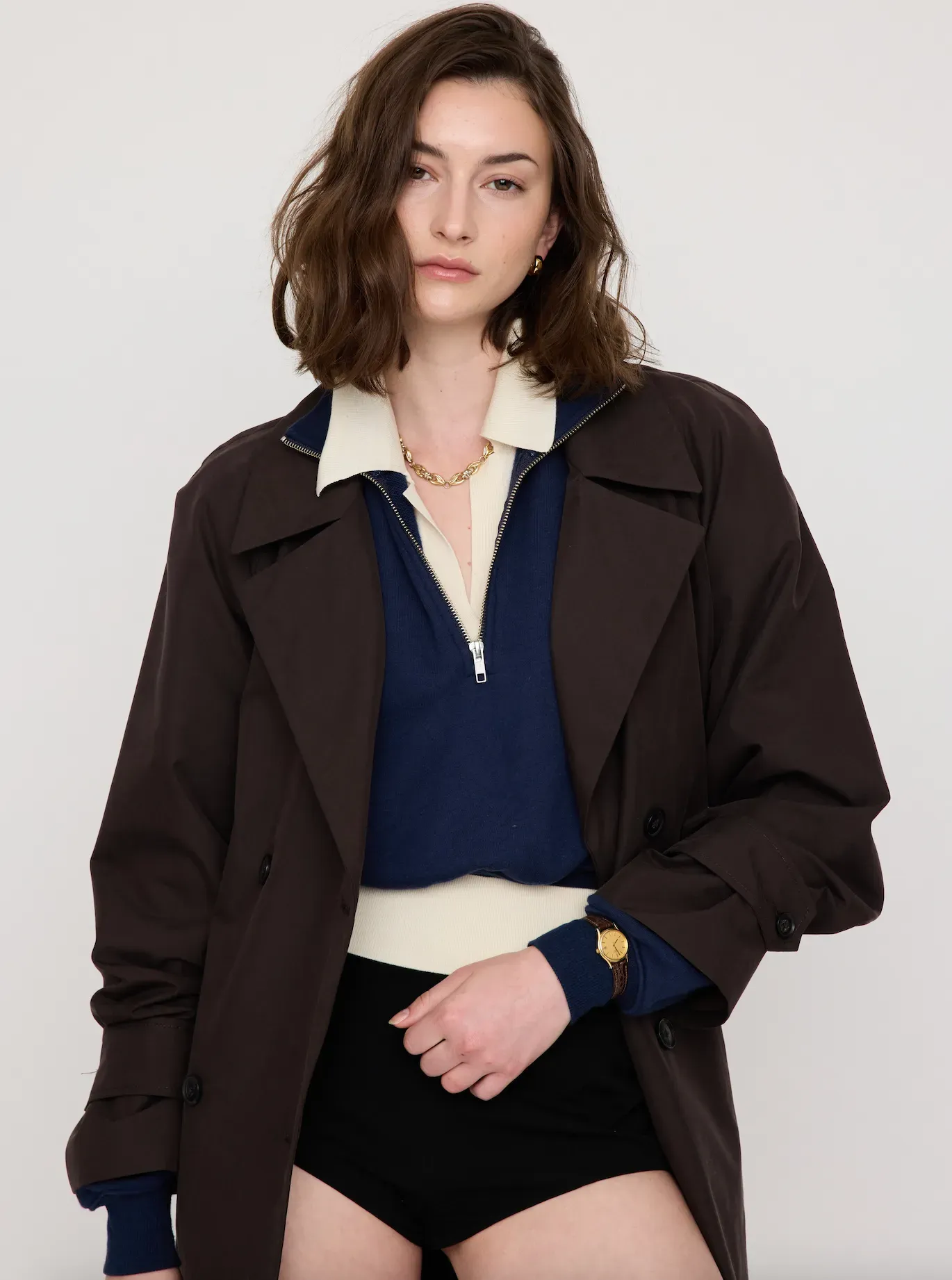 Model wearing a dark jacket over a navy top and black shorts, standing against a plain light background.