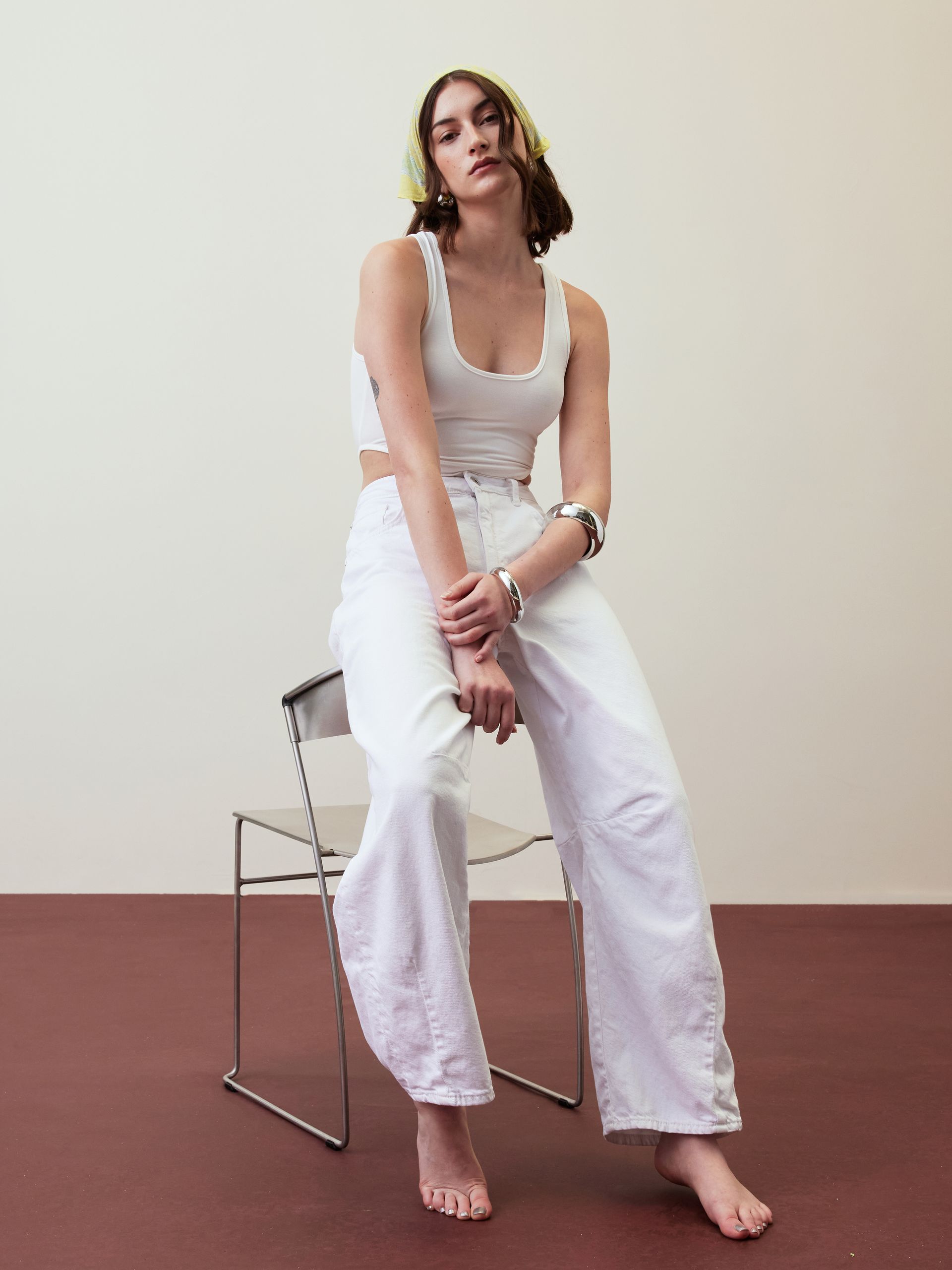 Woman in white sitting on a modern chair against a plain light background.