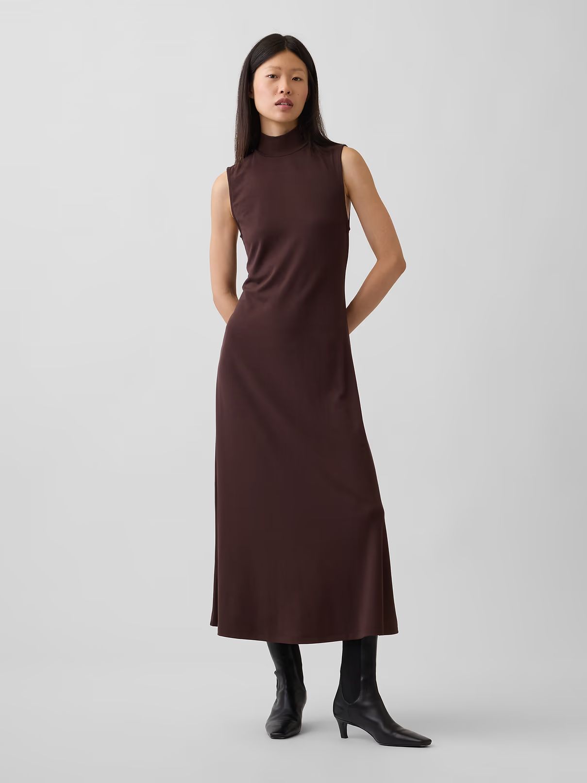 Model wearing a sleeveless burgundy maxi dress and black boots, standing against a white background