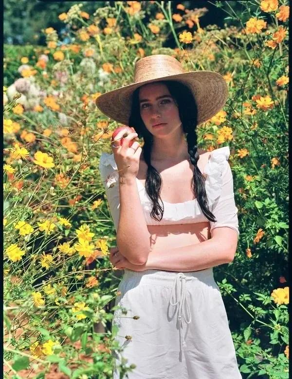Woman in a straw hat standing among yellow flowers, holding a blossom.