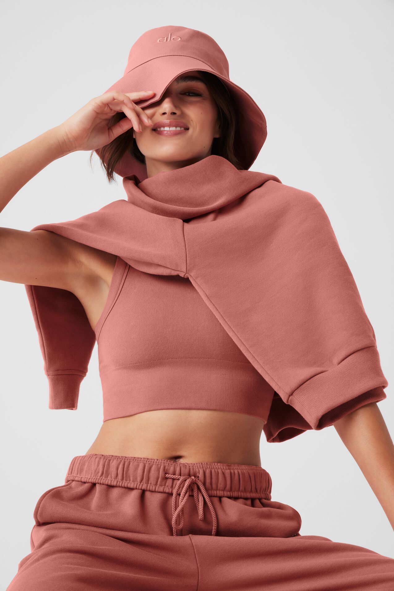 Woman in pink knit hat, scarf, and sleeveless top, smiling against a light background.