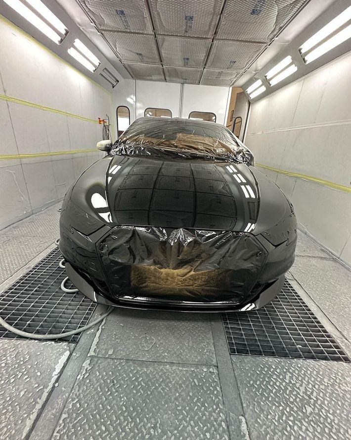 Auto nera in una cabina di verniciatura, ricoperta da pellicola protettiva.