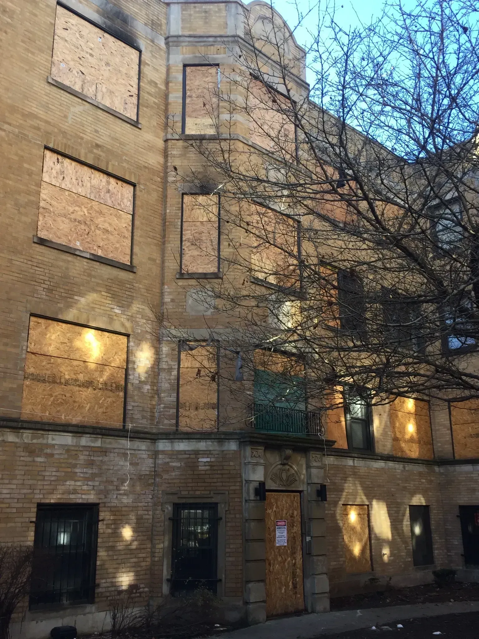 Boarded-up brick building with multiple boarded windows and a tree with bare branches.