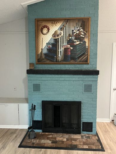 Light blue brick fireplace with black hearth and framed painting above it in a living room.