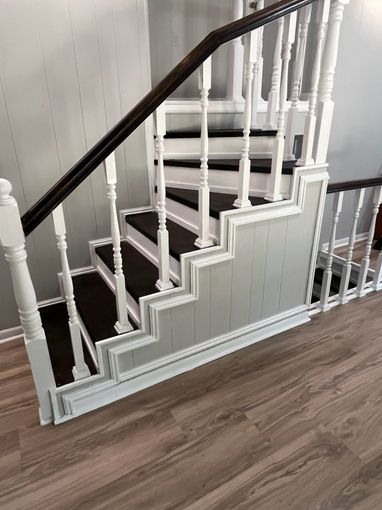 White staircase with dark wooden handrail and gray paneling in a home interior