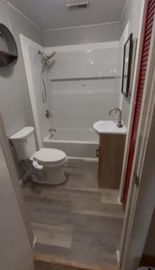 Narrow bathroom with tub-shower, toilet, and vanity sink in gray tones