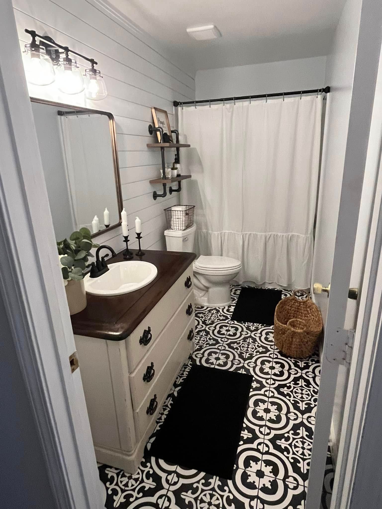 Small bathroom with white vanity, black-and-white rug, shower curtain, and woven hamper.