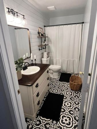 Small bathroom with white vanity, black-and-white rug, shower curtain, and woven hamper.