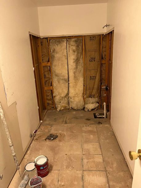 Narrow hallway under renovation with exposed studs, insulation, and debris on the floor.