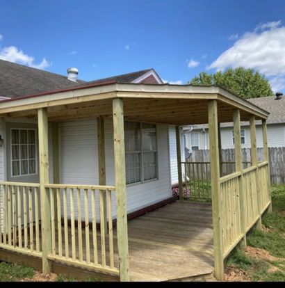 Covered wooden porch with railings attached to a white house under a blue sky.