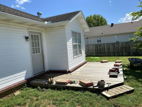 White house exterior with a small raised deck under construction in a sunny backyard