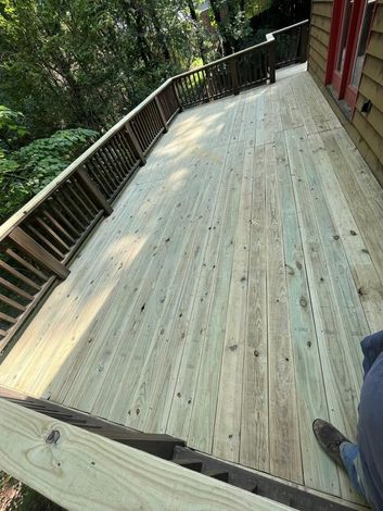 Wooden deck with railing beside a red house, overlooking a wooded area