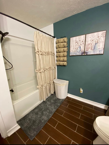 Small bathroom with shower-tub, beige curtain, teal wall, wood-look floor, and laundry hamper
