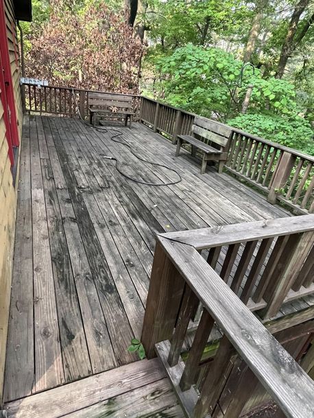 Weathered wooden deck with railing and benches overlooking a wooded area