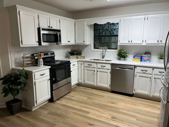 Bright white kitchen with stainless appliances, wood floor, and a small window over the sink