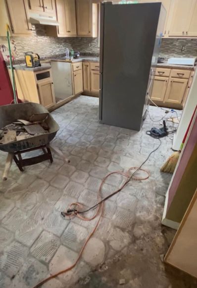Messy kitchen with a refrigerator in the middle, cords on the floor, and cabinets partially torn out