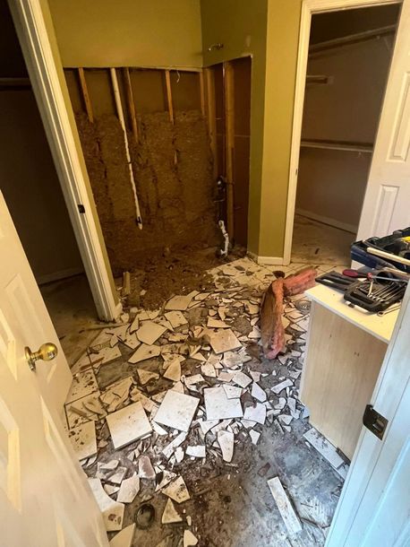 Bathroom with torn-up floor tiles and exposed wall studs, showing major renovation or damage.