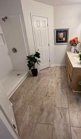 Bright bathroom with gray tile floor, white door, potted plant, and wood vanity with flowers.