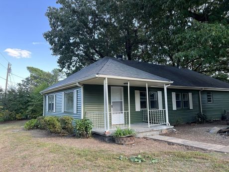 Small green house with a front porch and trees, viewed from the yard.