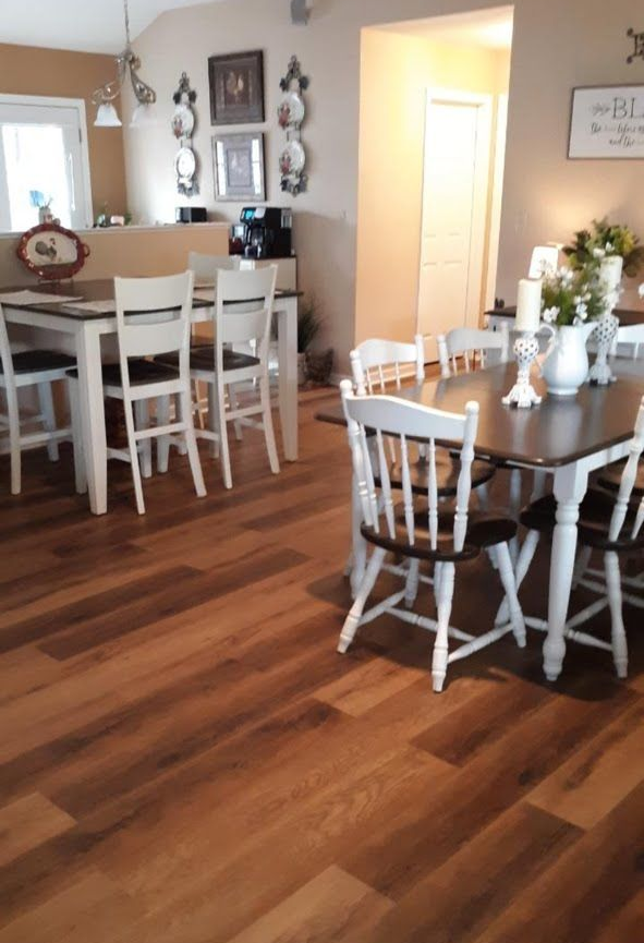 Bright dining room with wood floors, white chairs, and two tables with decor and flowers