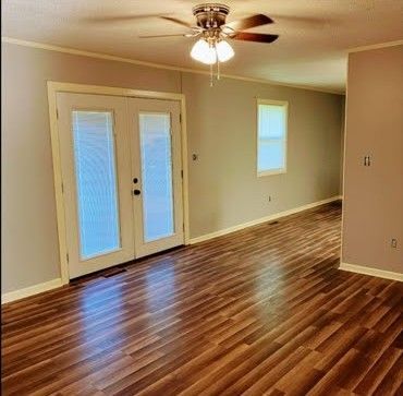 Empty living room with hardwood floors, ceiling fan, French doors, and a small window.