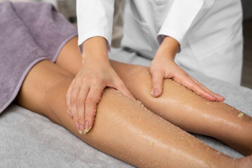 Massage therapist rubbing lotion on a client’s legs in a spa setting