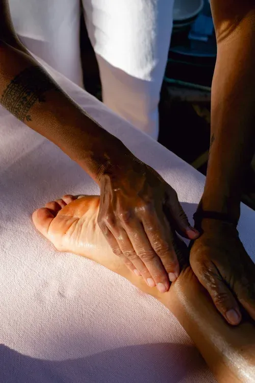 Hands massaging a person's calf on a treatment table under soft light