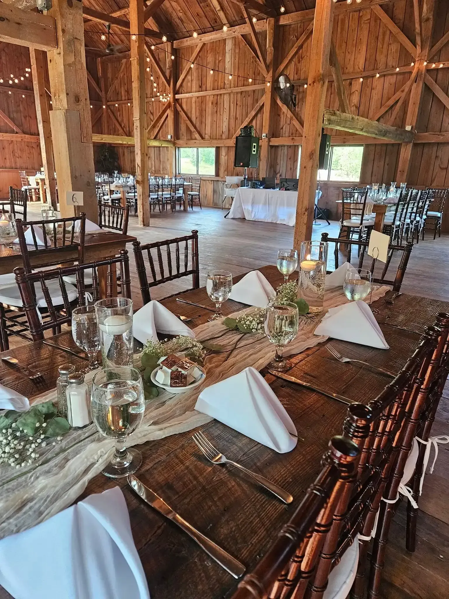 Rustic barn venue with long banquet tables set with white napkins, glassware, and floral centerpieces