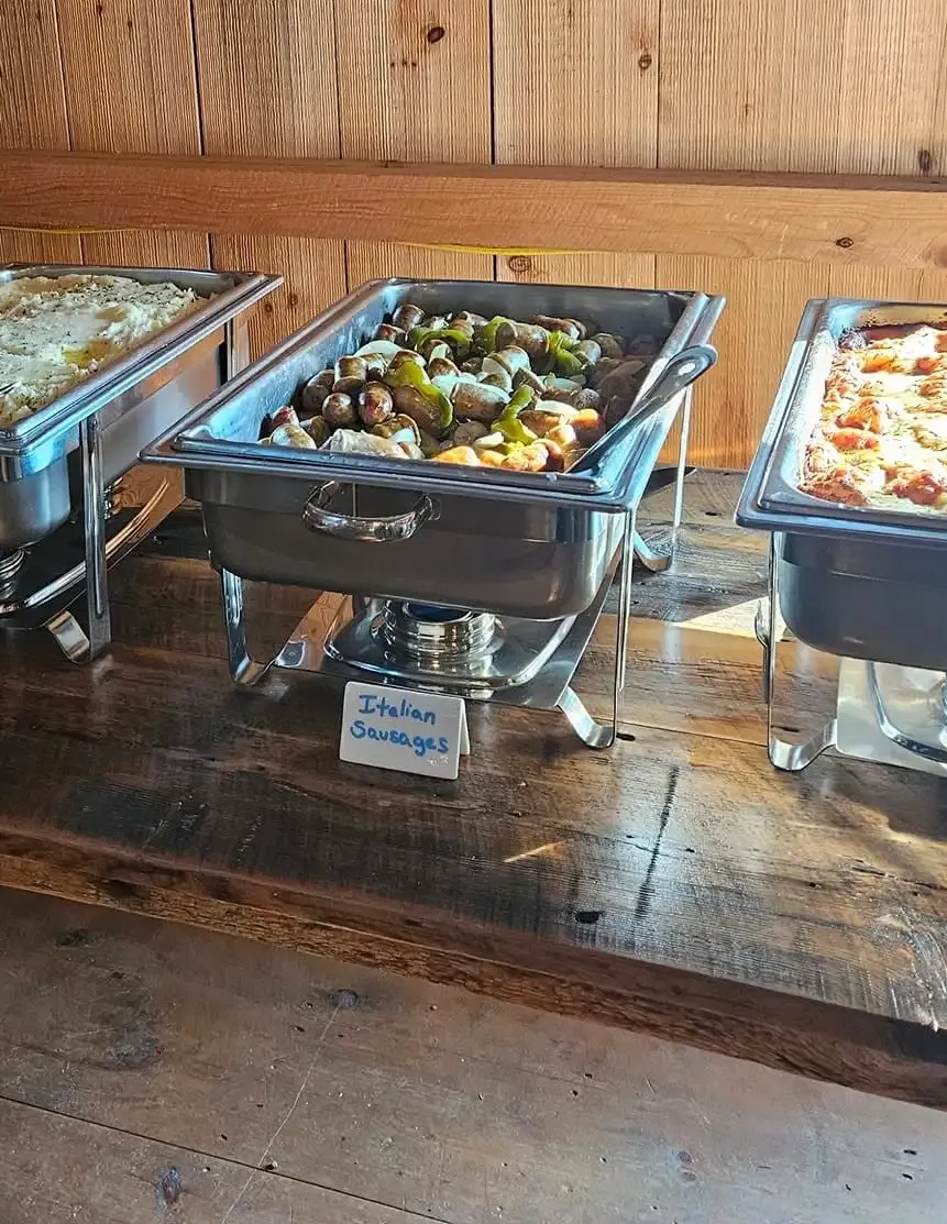 Buffet chafing dish with roasted vegetables on a wooden counter in a rustic dining area