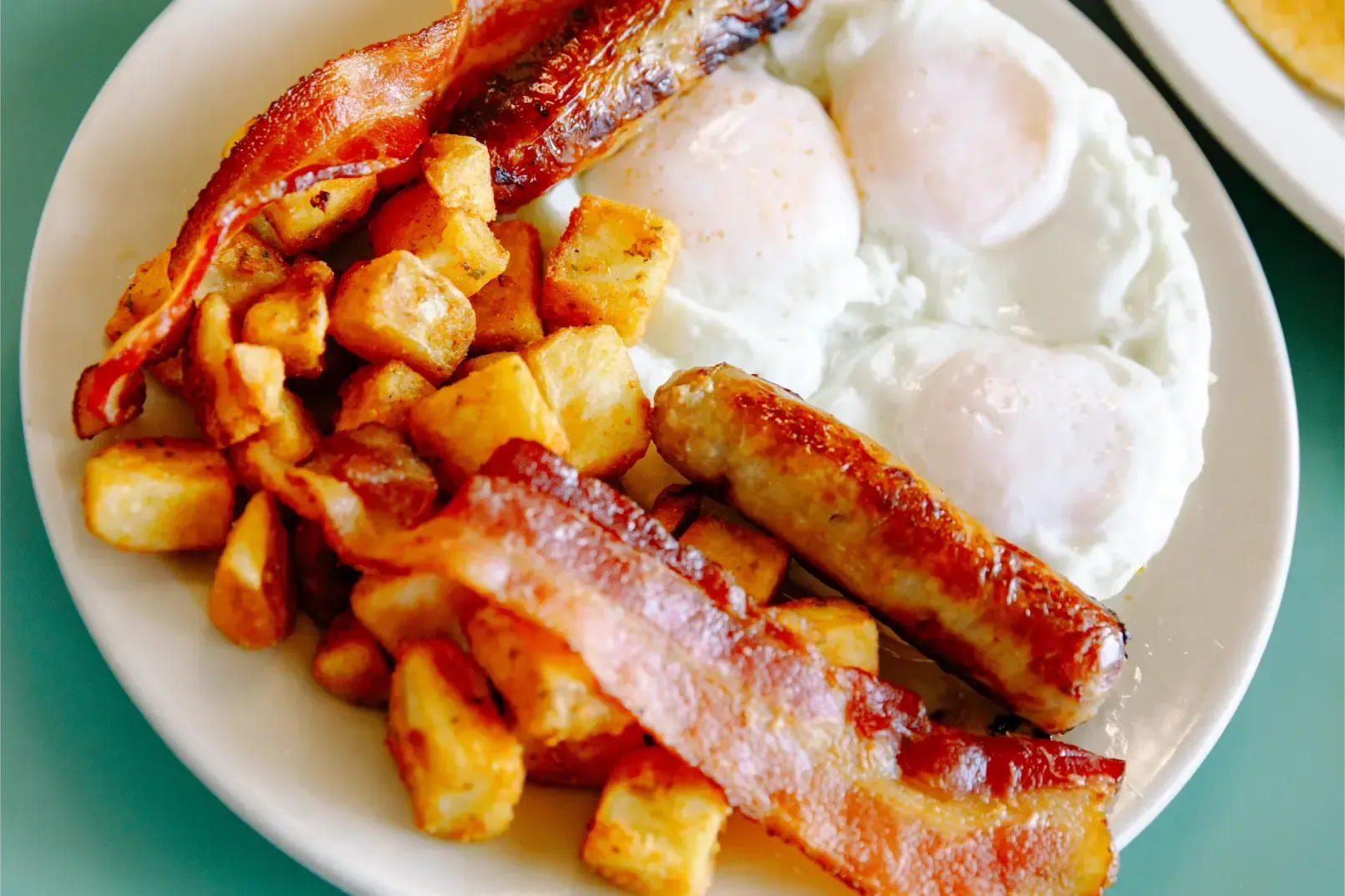 Plate of sausages, bacon, fried eggs, and diced potatoes on a white dish