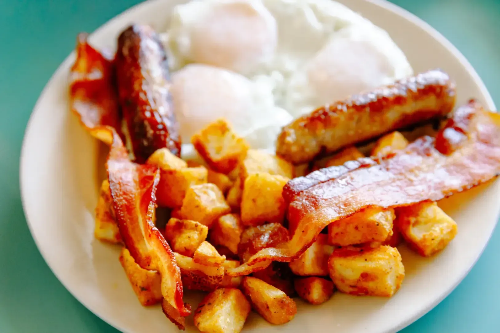 Plate of bacon, fried potatoes, and eggs on a white dish