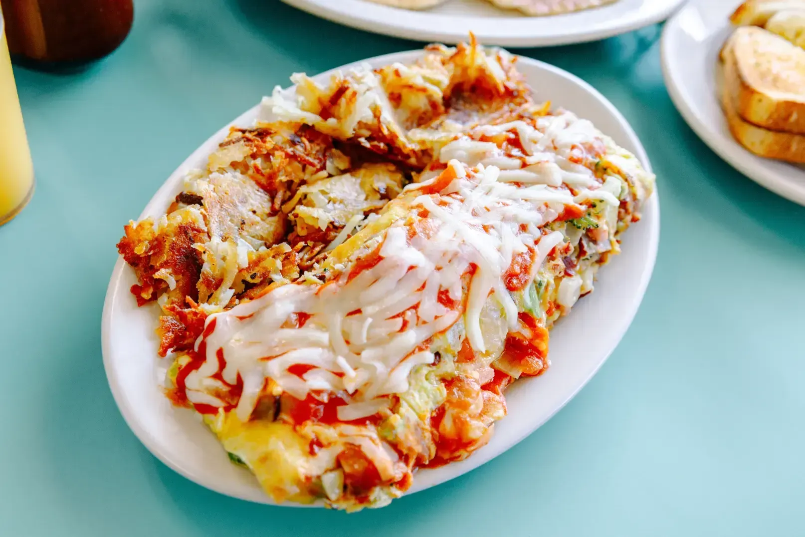 Cheesy baked pasta in a white oval dish on a turquoise table, with bread rolls nearby