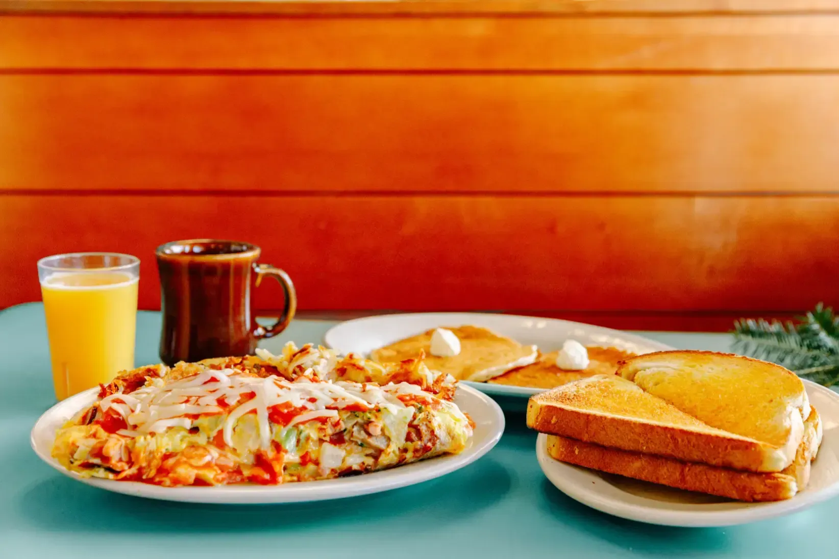 Breakfast spread with orange juice, coffee, pizza, and a toasted sandwich on a table