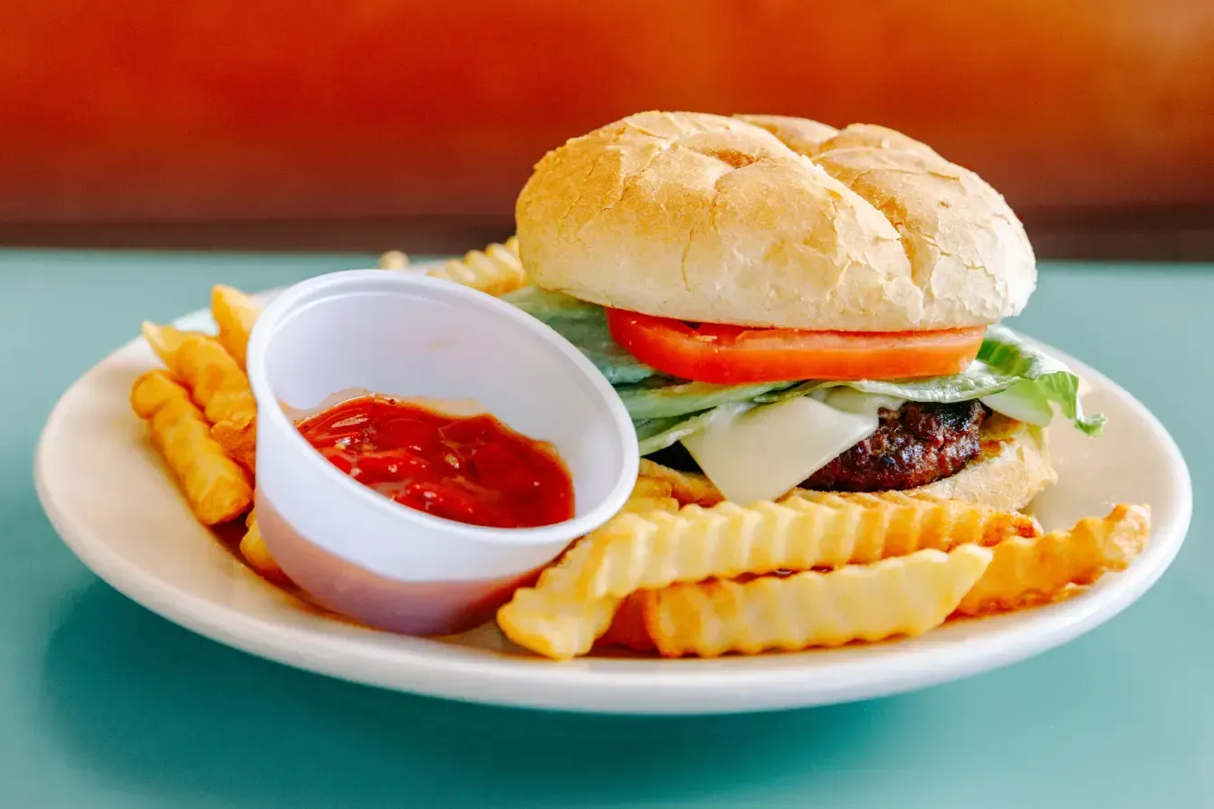 Sandwich with tomato, lettuce and meat on a plate with fries and a cup of ketchup