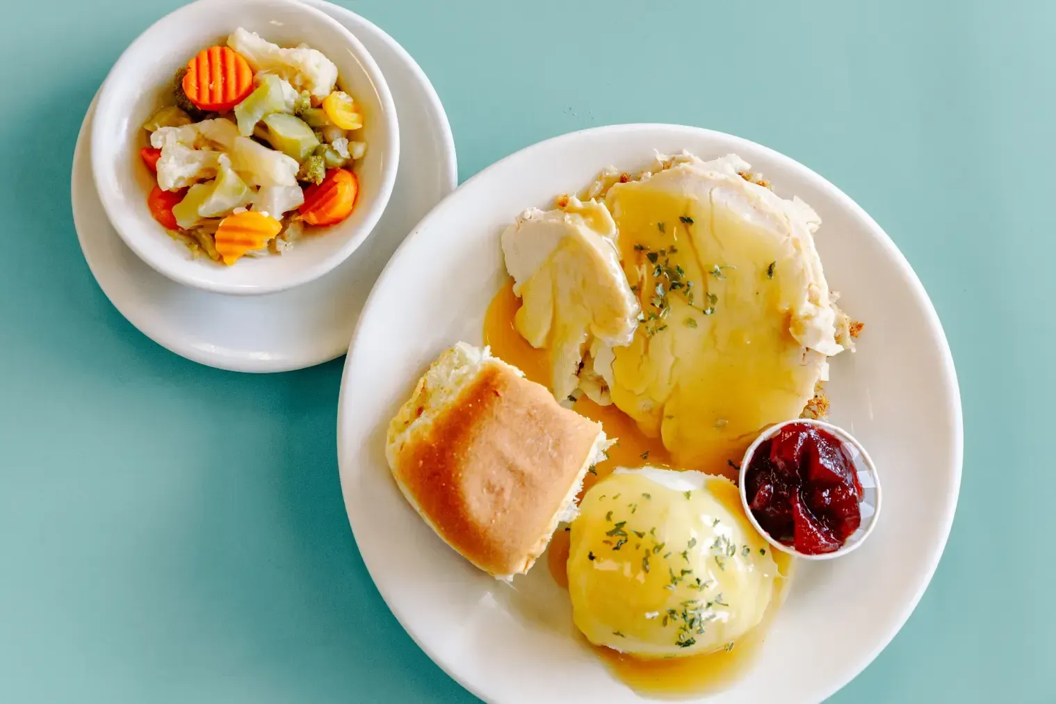 Two plates of breakfast pastries and fruit on a mint-green table