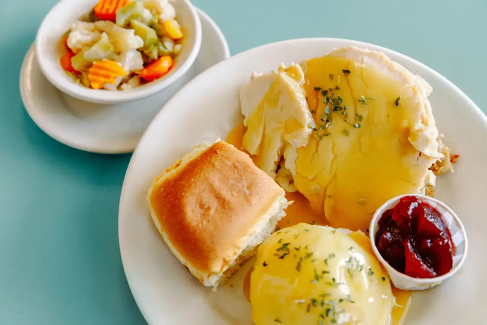 Breakfast plate with biscuits, eggs, jam, and a side bowl of mixed fruit on a teal table