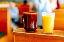 Two drinks on a wooden table: a brown mug and a clear glass of orange juice