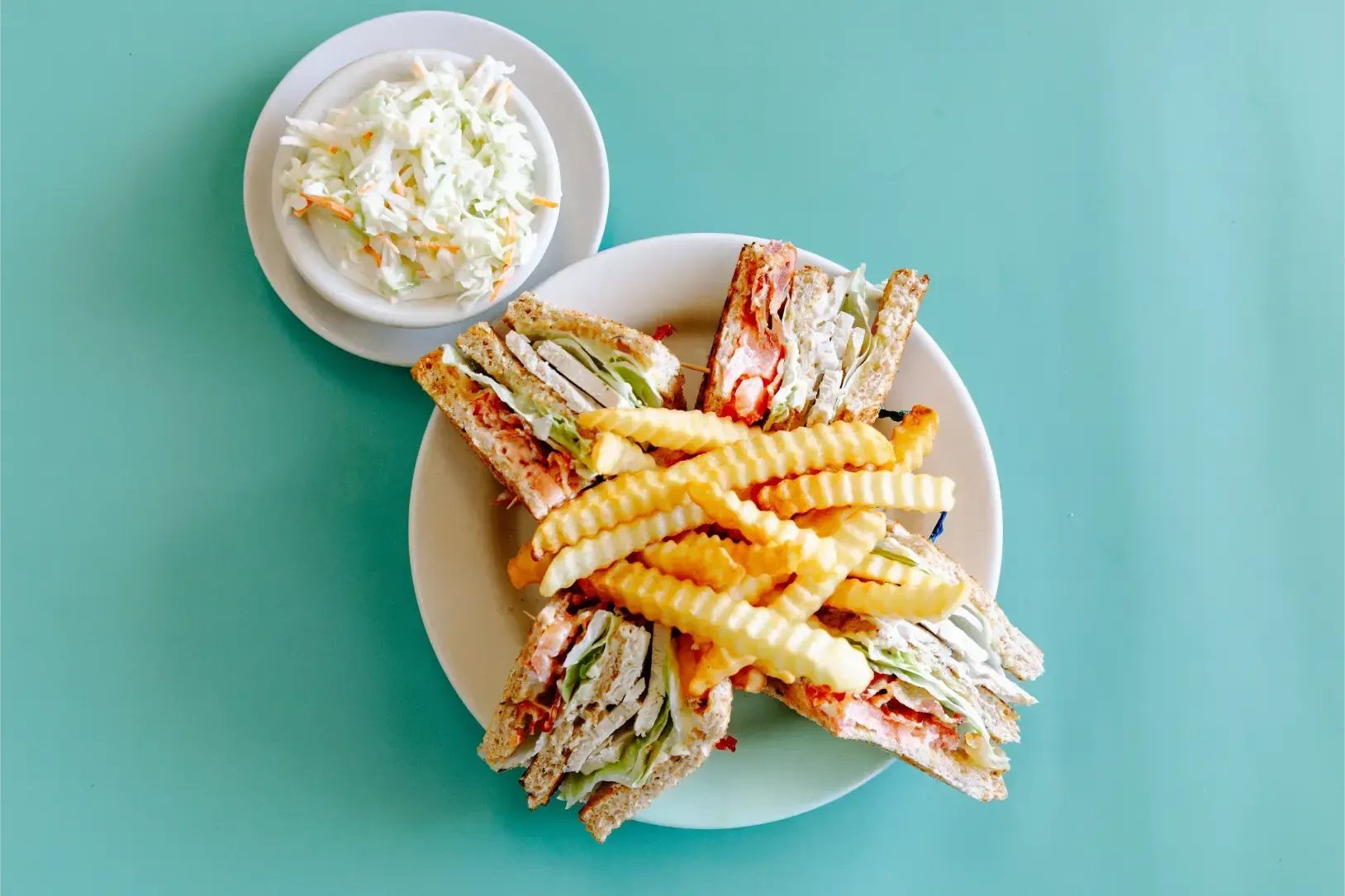 Sandwiches and crinkle fries on a plate with a side of coleslaw on a teal table